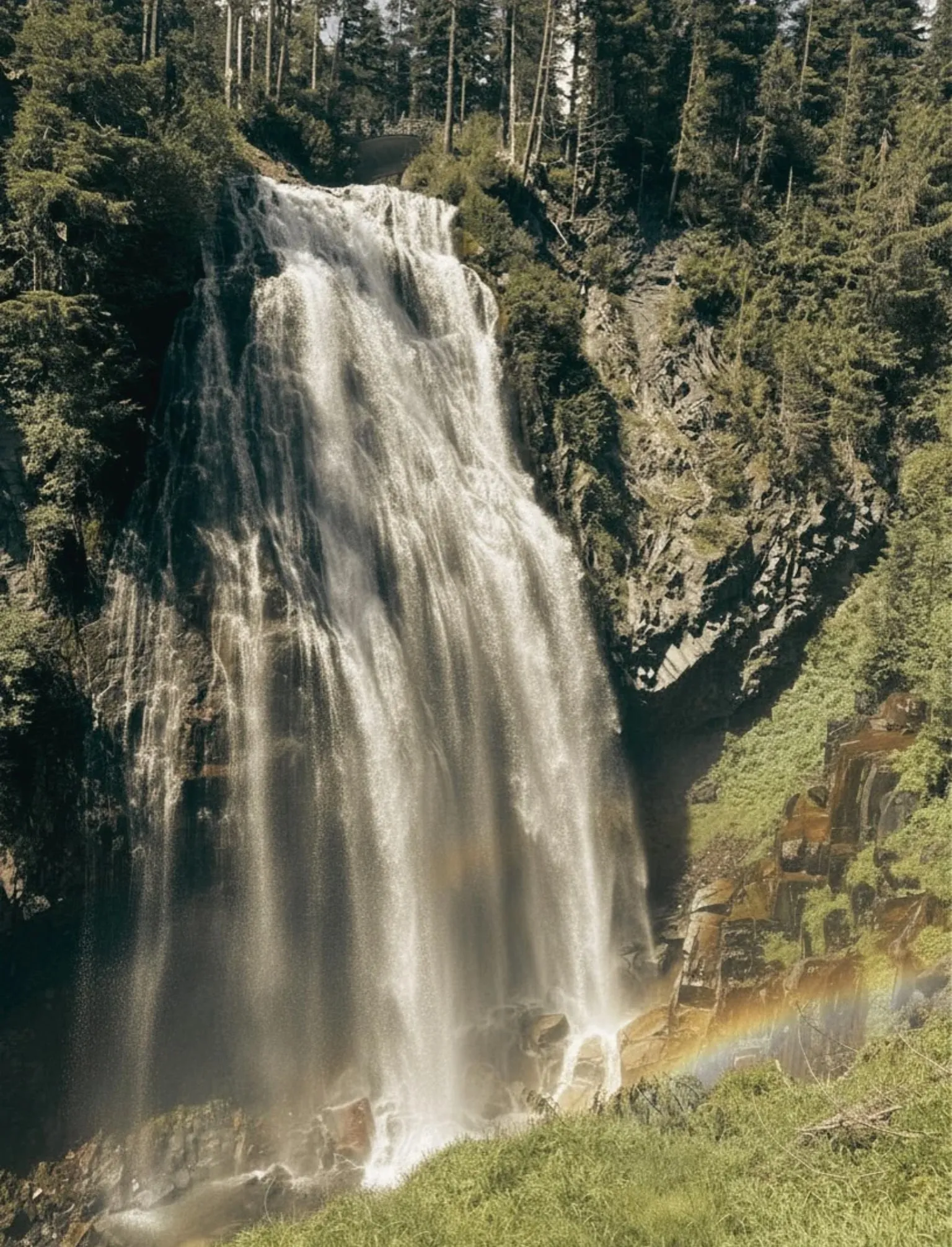 Narada Falls pouring down a dark rock face with a rainbow in the spray