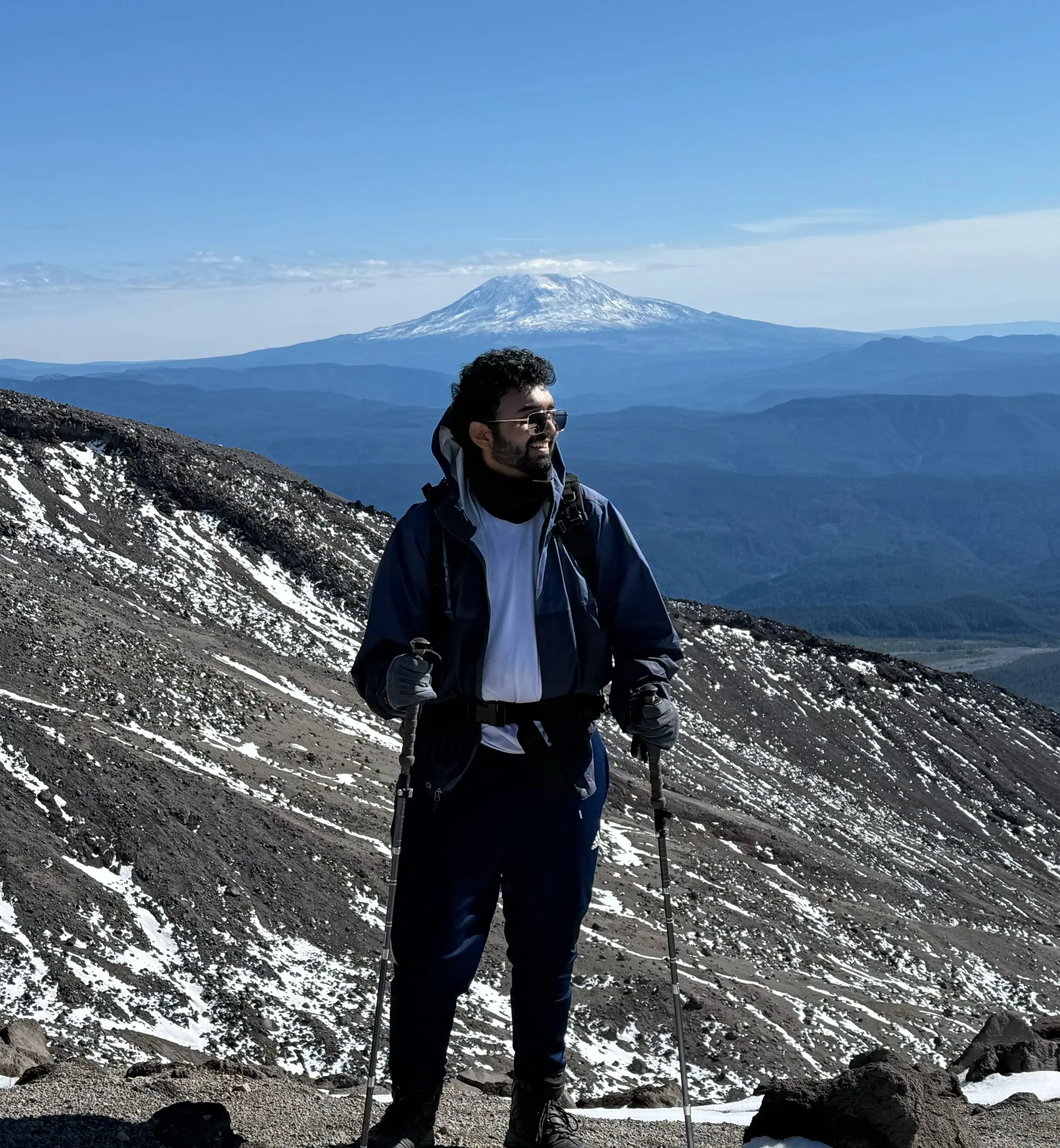 Abhishek on Monitor Ridge, Mount St. Helens, with snowfields and a distant volcano behind him